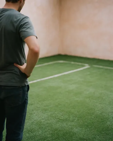 Un client de dos observe le nouveau court de tennis vert avec lignes blanches et murs en terre cuite.