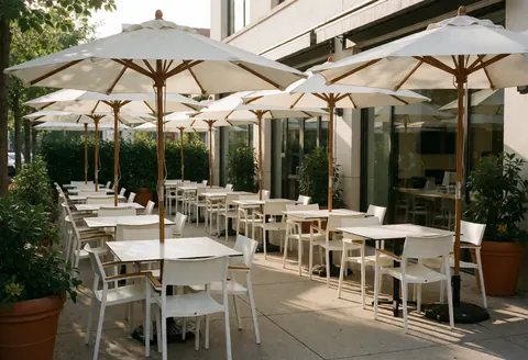 Terrasse d'un parc à thème avec tables blanches, parasols et plantes en pot éclairées par la lumière dorée du coucher de soleil.