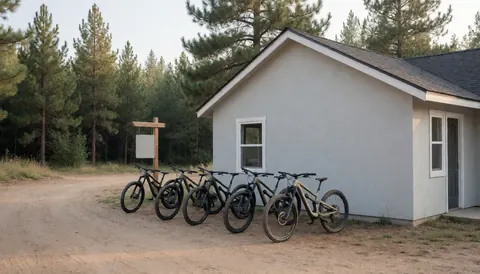 Vélos de montagne stationnés sur un terrain dégagé devant une petite maison en bois entourée de pins, idéal pour un coach de vélo de montagne.