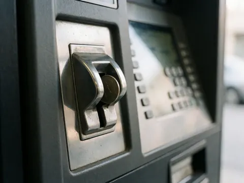 Détail d'une borne de stationnement avec une pièce métallique partiellement insérée dans la fente, le clavier et l'écran sont visibles en arrière-plan.