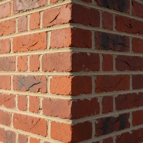 Mur de briques rouges avec mortier bien appliqué, coin vertical, lumière solaire, idéal pour entreprise de maçonnerie.