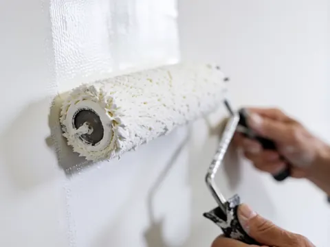 Mains utilisant un rouleau pour appliquer de la peinture blanche sur des murs blancs. Détail de la texture et de la lumière, pour la réparation de murs.