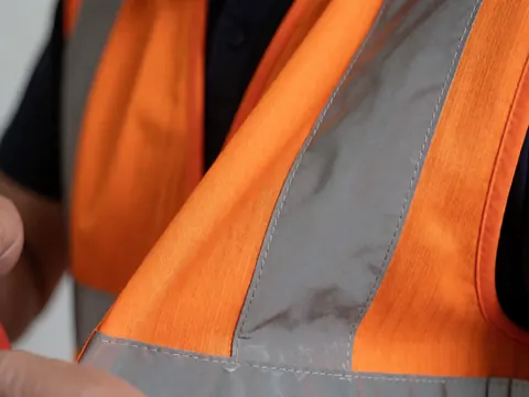 Gros plan sur un gilet de sécurité orange montrant les coutures et les bandes réfléchissantes métalliques, idéal pour les activités de plein air et le camping.
