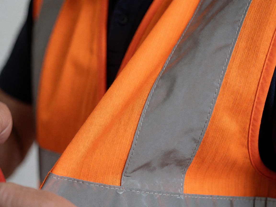 Gros plan sur un gilet de sécurité orange montrant les coutures et les bandes réfléchissantes métalliques, idéal pour les activités de plein air et le camping.