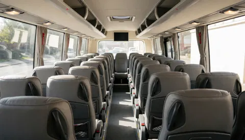 Vue intérieure d'un bus de tourisme montrant des rangées de sièges gris, un couloir central et la lumière naturelle pénétrant par les grandes fenêtres latérales.