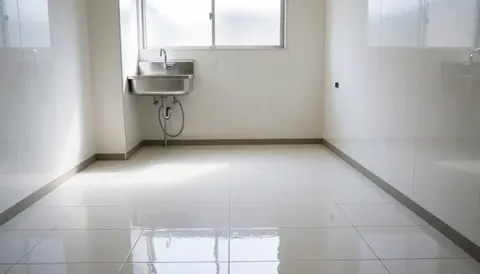 Espace propre et professionnel pour installation de cuisine, avec évier en acier inoxydable, sol de carreaux blancs brillants et fenêtre haute laissant entrer la lumière naturelle.