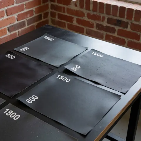 Papier abrasif automobile grain 800 et 1500 posé sur une table sombre avec un mur de briques rouges en arrière-plan pour la réparation de carrosserie