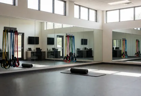 Salle de sport vide équipée de miroirs, de bandes de résistance et de rouleaux de mousse sur un sol en caoutchouc, idéale pour un instructeur de golf.