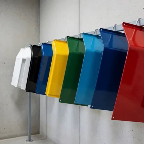Métaux récemment peints aux couleurs éclatantes suspendus sur une étagère métallique, avec des murs en béton poli et un fini industriel soigné.