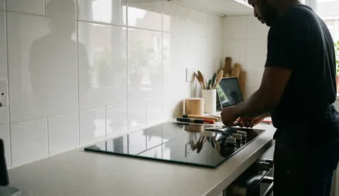 Technicien installe une cuisinière en verre dans une cuisine moderne avec des murs carrelés blancs et des outils visibles.