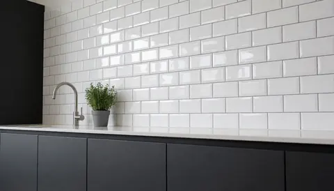 Cuisine moderne équipée de carreaux muraux blancs brillants, de placards gris et d'un évier avec robinet en acier inoxydable.
