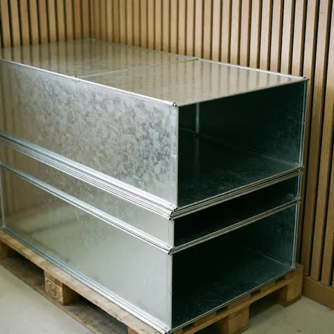 Tuyaux métalliques galvanisés empilés sur une palette en bois avec des murs en lattes de bois et une lumière naturelle, produit pour entreprise de poinçonnage métallique