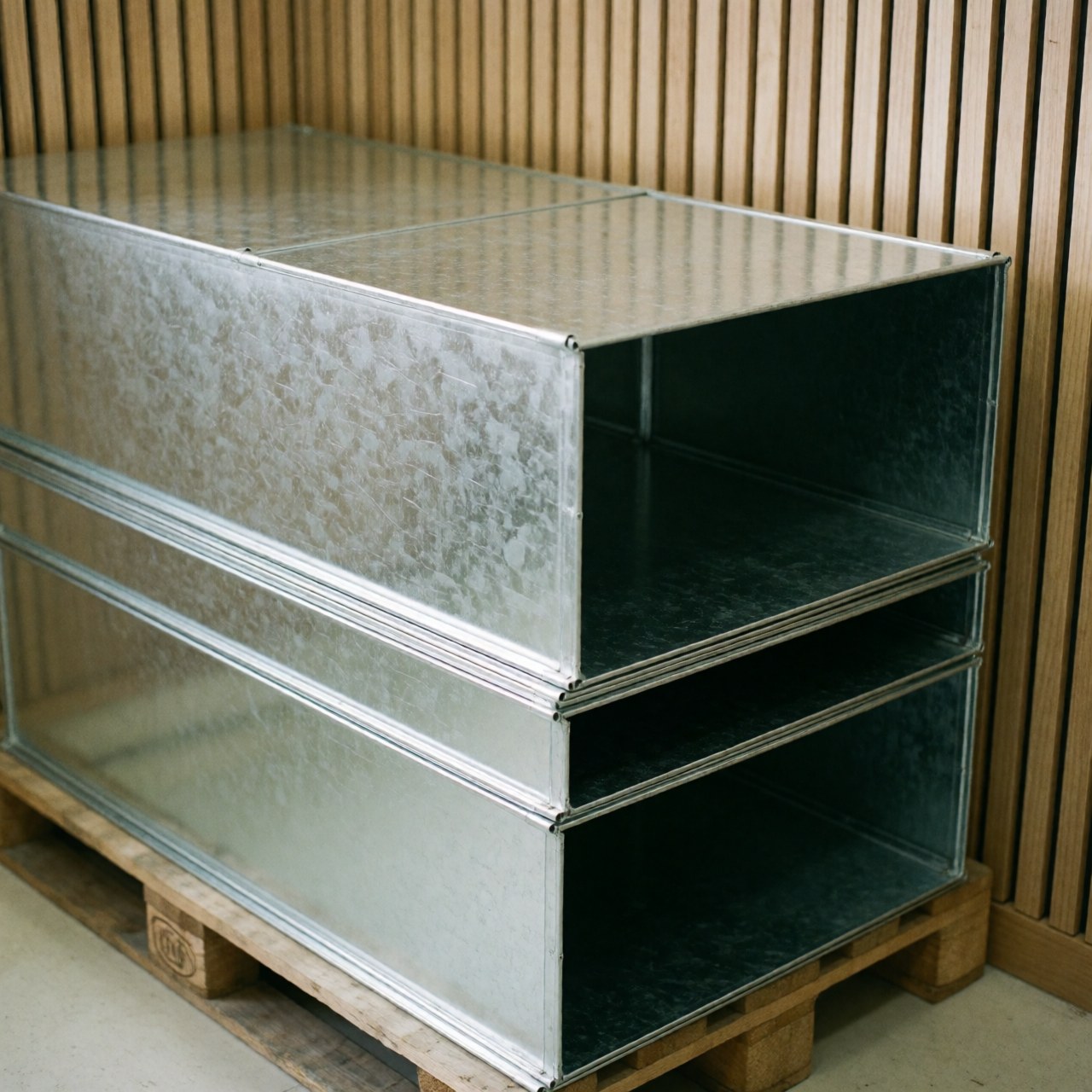 Tuyaux métalliques galvanisés empilés sur une palette en bois avec des murs en lattes de bois et une lumière naturelle, produit pour entreprise de poinçonnage métallique