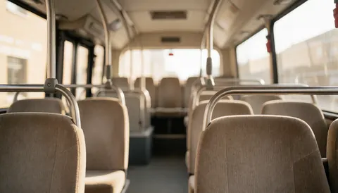 Intérieur d'un autocar touristique avec des sièges beiges et des barres métalliques, éclairage chaleureux et arrière-plan flou, idéal pour ajouter du texte.