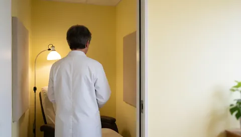 Professionnel de dos dans une salle d'hypnothérapie avec chaise longue, panneaux acoustiques, murs jaunes et lumière d'appoint.