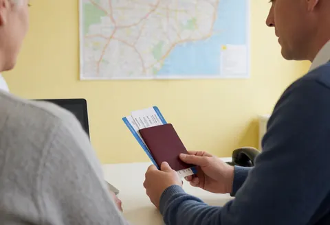 Un agent de bureau examine les documents de voyage d'un client devant une carte murale pour assurer le bon déroulement du service.