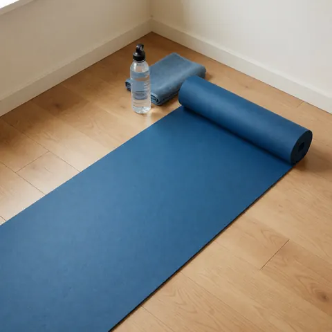 Tapis de yoga bleu posé sur un plancher en bois clair, accompagné d'une bouteille d'eau et d'une serviette bleue dans le coin, idéal pour le fitness à domicile.