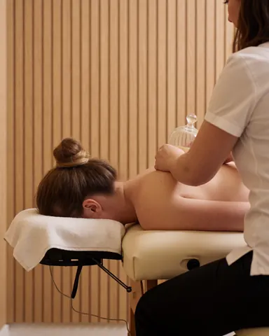 Un thérapeute applique des ventouses sur le dos d'un client allongé sur une table de massage dans un cabinet aux murs en bois clair.