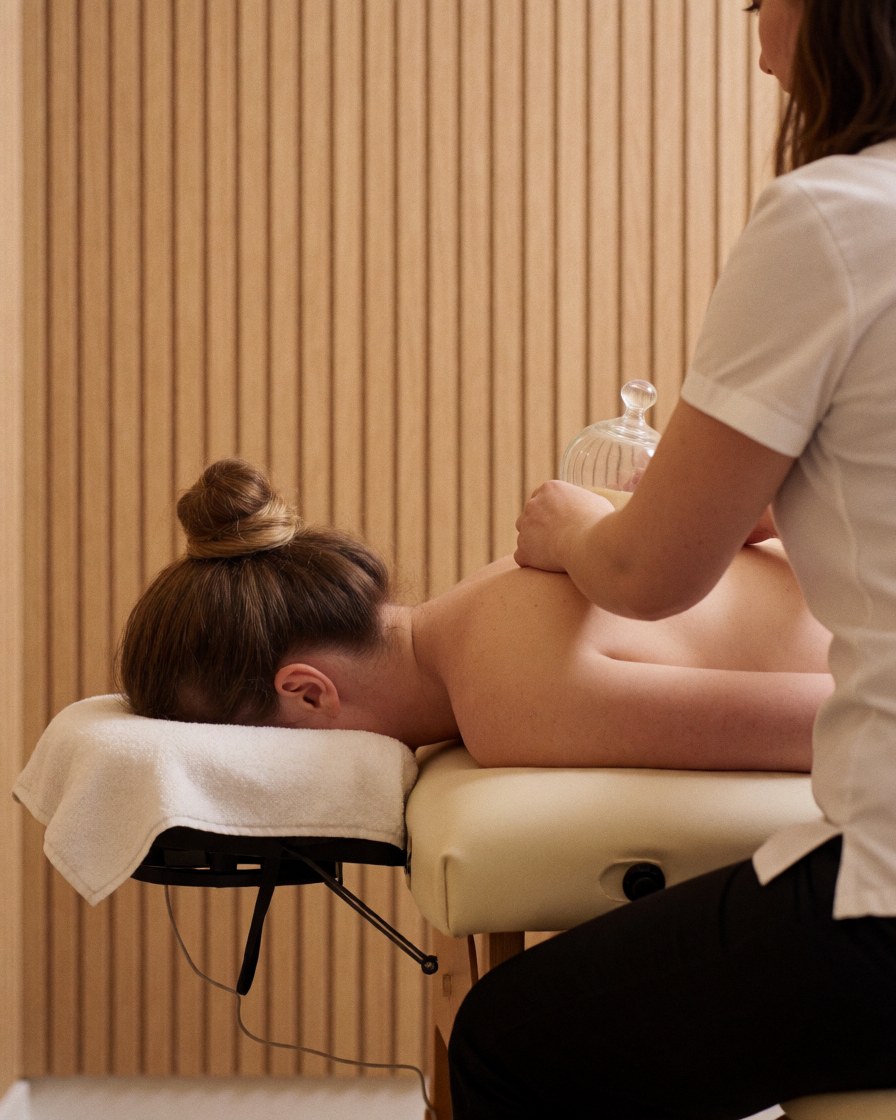 Un thérapeute applique des ventouses sur le dos d'un client allongé sur une table de massage dans un cabinet aux murs en bois clair.