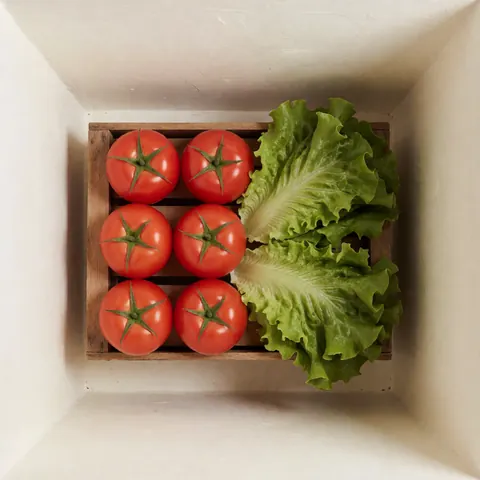 Vue de dessus d'une caisse en bois remplie de tomates rouges et de laitue verte fraîche, idéale pour un catalogue de produits alimentaires.