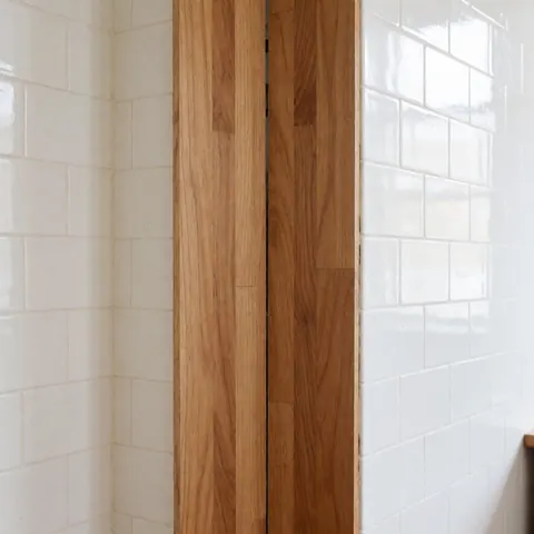 Détail de sol en bois avec des joints parfaits et des murs recouverts de carreaux blancs brillants, idéal pour un professionnel de la pose de sols.