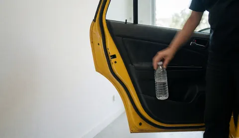 Une main prend une bouteille d'eau dans la poche de porte d'un taxi jaune sur fond blanc avec espace pour texte.