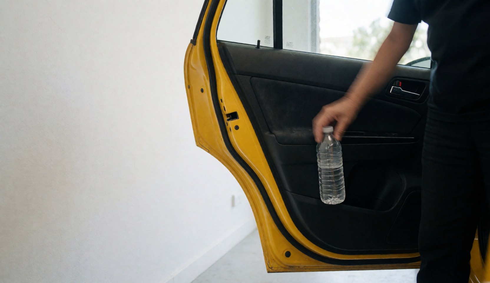 Une main prend une bouteille d'eau dans la poche de porte d'un taxi jaune sur fond blanc avec espace pour texte.