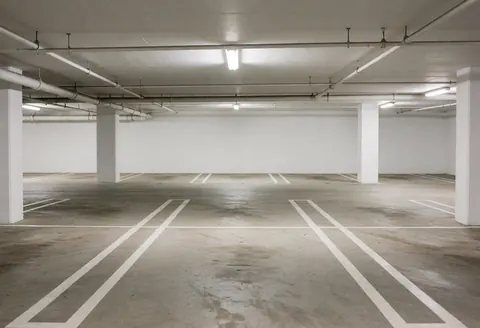 Parking souterrain vide avec sol en béton marqué, colonnes blanches et éclairage fluorescent, adapté aux entreprises.