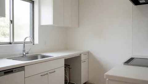 Cuisine contemporaine dotée d'un évier en acier inoxydable, de tuyaux de cuivre visibles et de murs blancs, idéale pour les plombiers.