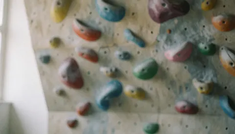 Fond de mur d'escalade artificiel avec des prises multicolores et une texture floue, idéal pour les textes sur l'entraînement à l'escalade.