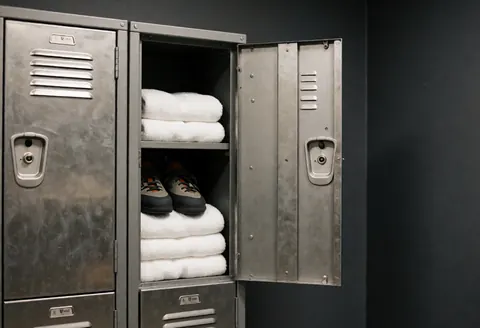 Coffre métallique ouvert avec chaussures de escalade et serviettes blanches, murs gris foncé, vestiaire de escalade propre