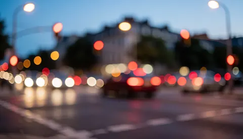 Fond urbain avec des lumières de circulation floues, des lampadaires et un ciel au crépuscule, idéal pour des textes liés au transport et à la logistique.