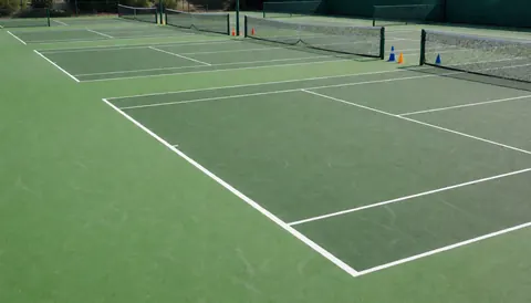 Vue de trois courts de tennis alignés avec des lignes blanches et des filets, surface en acrylique verte, idéale pour une école de tennis.