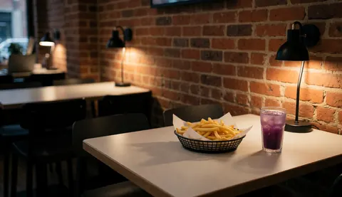 Table de restaurant avec frites dans un panier et boisson de maïs violet, mur de briques et lumières chaudes, idéal pour la couverture d'un restaurant de poulet.