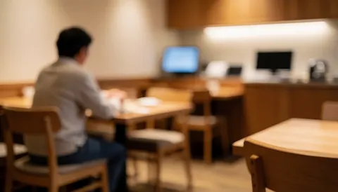 Vue d'un client assis dans un restaurant, entouré de tables et chaises en bois clair, éclairage chaleureux créant une atmosphère accueillante pour du texte.