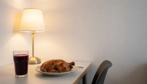 Assiette de poulet rôti accompagnée d'une boisson à base de maïs violet posée sur une table avec une lampe et un mur blanc, créant une ambiance chaleureuse.