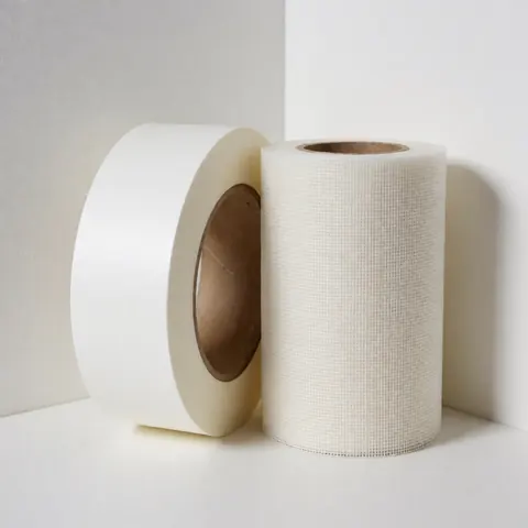Deux rouleaux de ruban adhésif, l'un en papier lisse et l'autre en malle, posés dans un coin blanc, destinés à la réparation de murs.