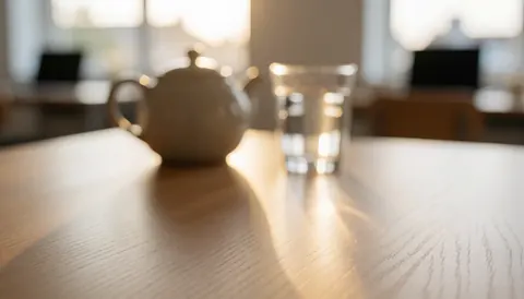 Table en bois avec théière en céramique et verre d'eau, éclairée par une lumière chaude, idéale comme fond pour spa ou massage.