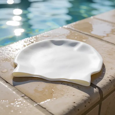 Un bonnet de natation blanc en silicone posé sur le rebord d'une piscine, idéal pour l'entraînement en club de natation.