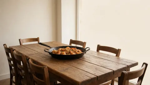 Crevettes cuites dans une poêle noire posée sur une table en bois rustique dans un restaurant aux murs blancs et aux chaises en bois.