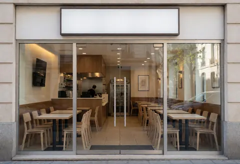 Entrée d'un restaurant moderne avec tables et chaises, une personne travaillant en cuisine, éclairage chaleureux.