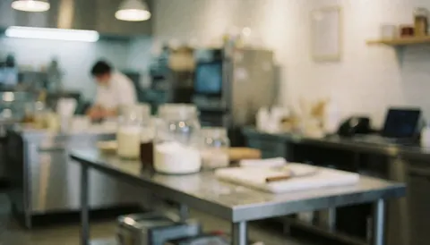 Cuisine de glacier avec tables en acier inoxydable, pichets en verre et personne travaillant en arrière-plan sous un éclairage doux